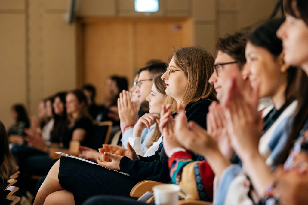 Grupa ludzi na konferencji, skupiona i bijąca brawo.