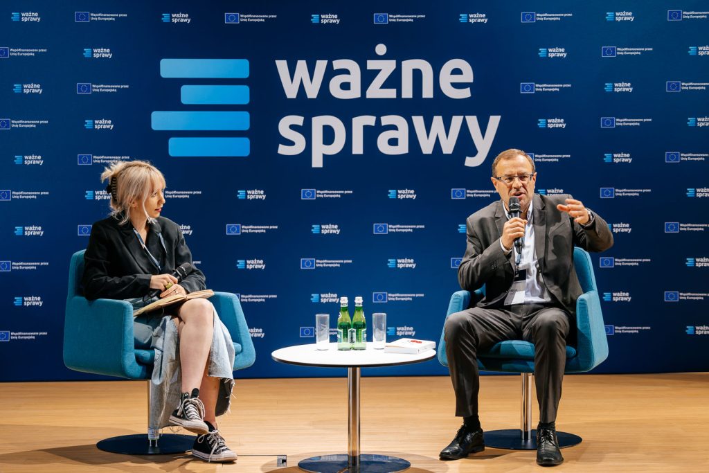 Dwoje ludzi na scenie podczas wydarzenia "Ważne Sprawy" z mikrofonem i logami w tle.