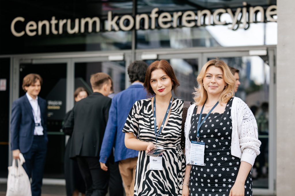 Grupa osób stojących przed wejściem do centrum konferencyjnego, dwie kobiety na pierwszym planie.