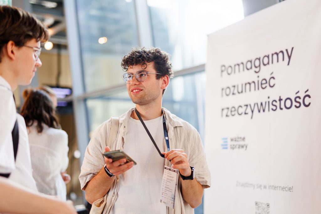 Młody uczestnik z telefonem przy roll-upie Ważne Sprawy „Pomagamy rozumieć rzeczywistość” – konferencja Stan Młodych 2025.