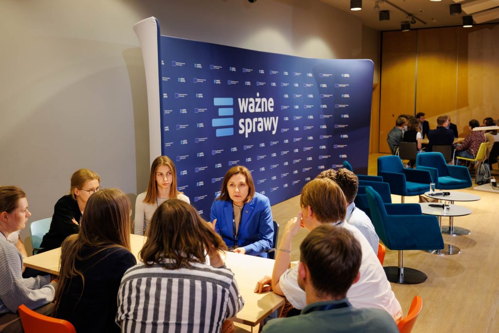 Młodzi uczestnicy rozmawiają przy stoliku podczas warsztatów na konferencji Stan Młodych, w tle baner Ważne Sprawy.