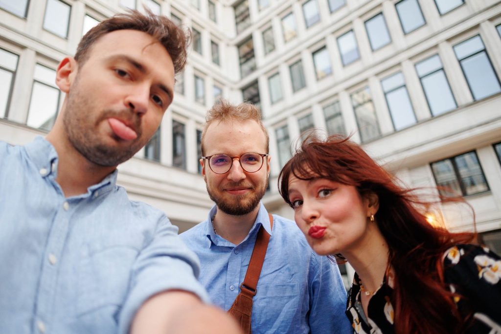 Troje uczestników robi zabawne selfie przed biurowcem – konferencja Stan Młodych 2025.