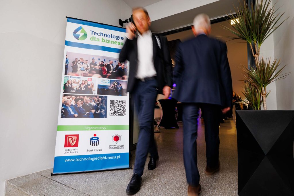 Uczestnicy przechodzą obok roll-upu konferencji Technologie dla Biznesu.