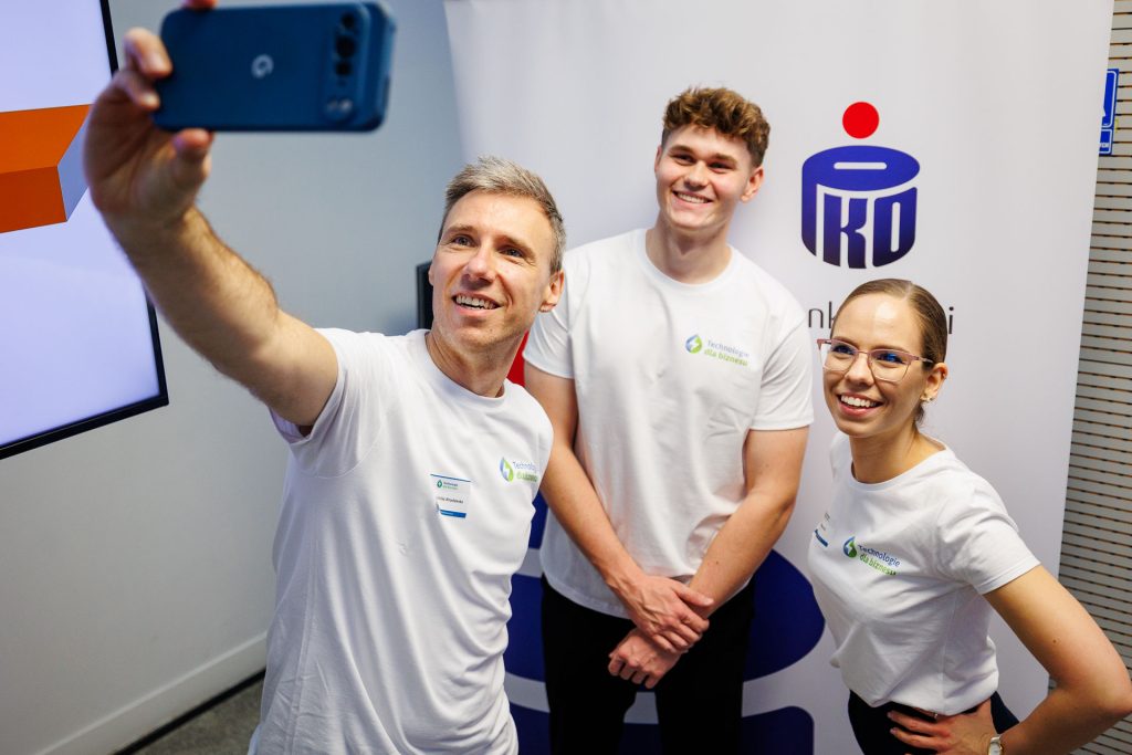 Mężczyzna robi selfie z dwojgiem wolontariuszy przed logo PKO Banku Polskiego na Technologie dla Biznesu.