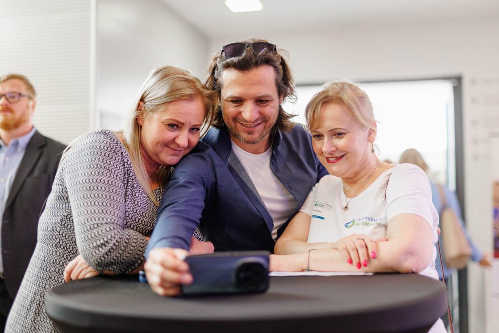 Troje uczestników ogląda zdjęcie na telefonie przy wysokim stoliku na konferencji Technologie dla Biznesu.