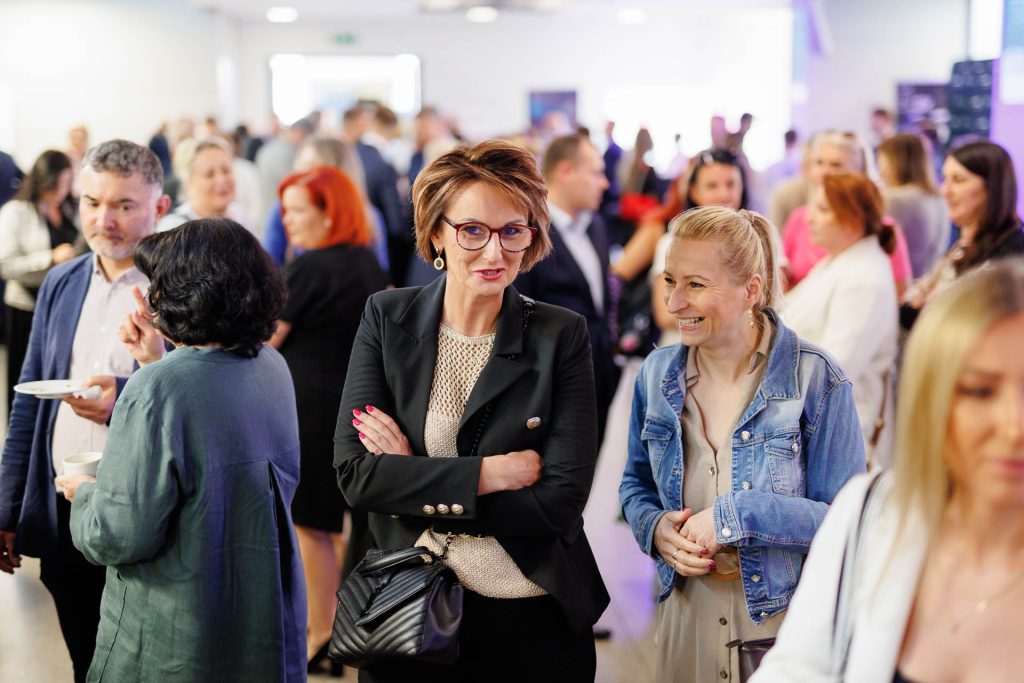 Uczestniczki konferencji Technologie dla Biznesu rozmawiają w zatłoczonym holu.