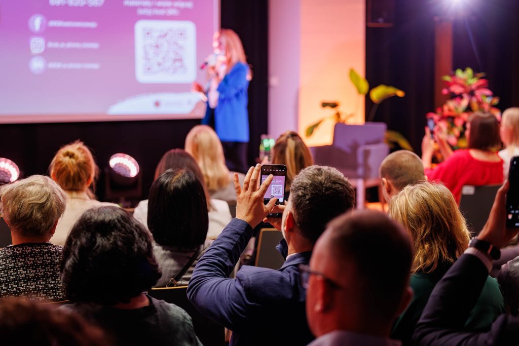 Uczestnicy fotografują telefonami ekran z kodem QR podczas wystąpienia na Technologie dla Biznesu.