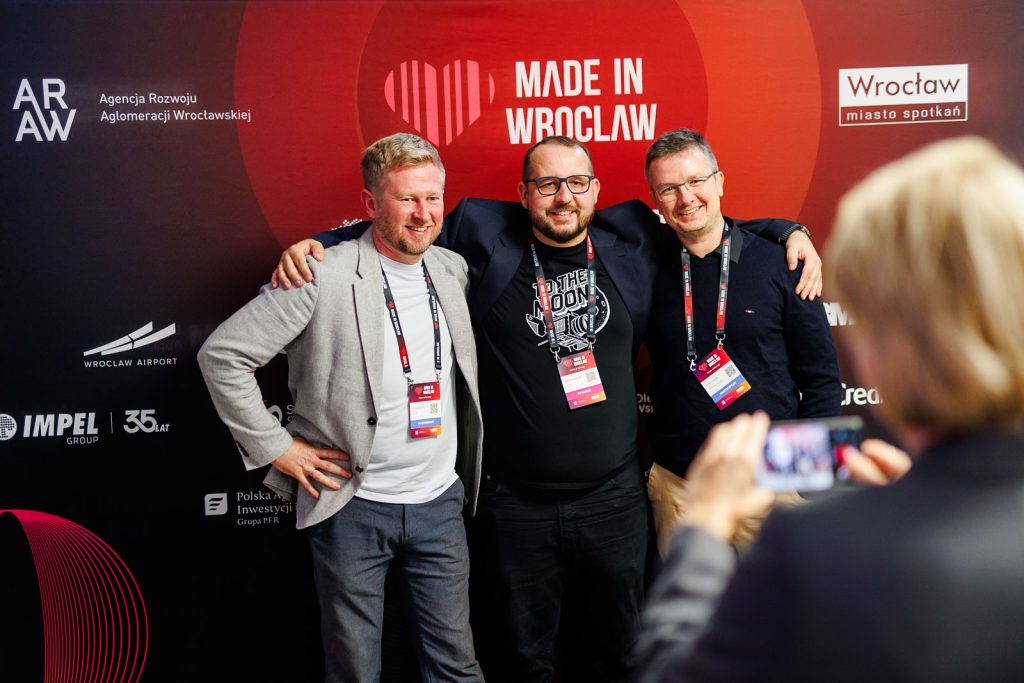 Uczestnicy Made in Wrocław 2025 pozują do zdjęcia na tle czerwonej ścianki z logo wydarzenia.
